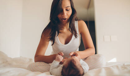 Frau sitzt auf dem Bett und spielt mit ihrem Baby zu Hause. Mutter und Sohn spielen im Schlafzimmer. - JLPSF27488