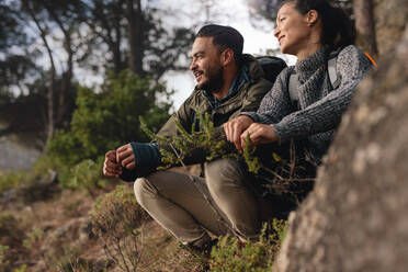 Couple taking a break after hiking uphill in the countryside. Young man and woman sitting on mountain and looking away. - JLPSF27495