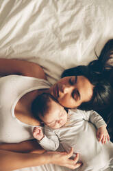 Draufsicht auf Mutter und Sohn, die zusammen auf dem Bett schlafen. Junge Frau mit einem neugeborenen Jungen im Bett zu Hause. - JLPSF27504
