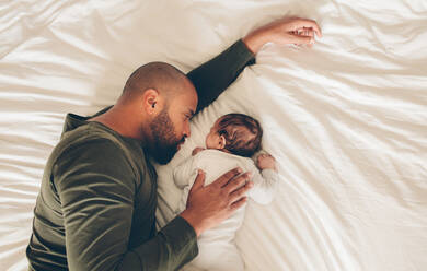 Draufsicht auf einen neugeborenen Jungen, der mit seinem Vater im Bett schläft. Vater und Sohn liegen zusammen im Bett. - JLPSF27506