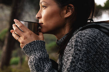 Nahaufnahme einer jungen asiatischen Wanderin beim Kaffeetrinken, die sich während einer Wanderung ausruht. - JLPSF27511