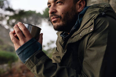 Nahaufnahme eines gutaussehenden jungen Mannes beim Kaffee trinken im Freien. Männlicher Wanderer, der sich ausruht und frischen Kaffee trinkt. - JLPSF27514