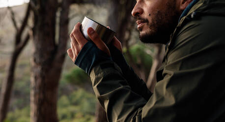 Nahaufnahme eines jungen männlichen Wanderers beim Kaffeetrinken. Ausgeschnittenes Bild eines männlichen Wanderers beim Ausruhen während einer Wanderung. - JLPSF27517