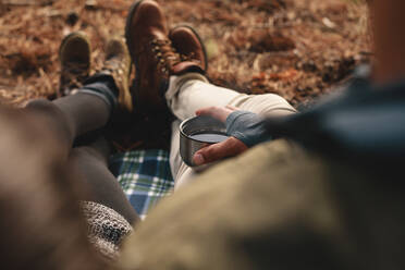 Close up of hiker couple sitting together outdoors with cup of coffee. Focus on hands holding cup of coffee. - JLPSF27521