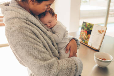 Nahaufnahme einer Frau mit Kind in der Küche zu Hause. Neugeborener Junge schläft in den Händen seiner Mutter. - JLPSF27524