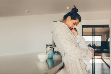 Frau im Bademantel hält ihren Sohn in der Küche zu Hause. Neugeborener Junge schläft in den Händen seiner Mutter. - JLPSF27525