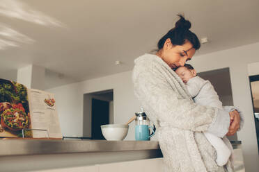 Liebevolle Mutter, die ihren neugeborenen Jungen trägt und in der Küche steht. Frau im Bademantel hält ihren schlafenden Sohn. - JLPSF27526
