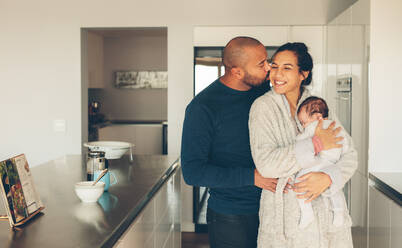 Liebevolles junges Paar mit ihrem neugeborenen Jungen in der Küche. Schöne junge Familie mit drei Kindern am Morgen in der Küche. - JLPSF27531