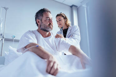 Krankenhausaufenthalt eines Mannes, der von einer Ärztin untersucht wird. Ein Arzt prüft den Herzschlag eines männlichen Patienten im Krankenhauszimmer. - JLPSF27562