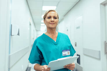 Porträt einer reifen Krankenschwester, die im Krankenhaus arbeitet. Eine Frau im Gesundheitswesen mit einem Klemmbrett im Flur. - JLPSF27569