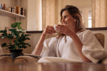 Lächelnde Frau im Bademantel auf einem Stuhl sitzend und Kaffee trinkend im Wellnessbereich. Frau trinkt Kaffee und entspannt sich im Wellnessbereich. - JLPSF27577