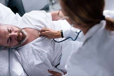 Blick von oben auf einen Arzt, der die Herzschläge eines kranken Patienten misst. Ein Mann im Krankenhaus wird von einer Ärztin untersucht. - JLPSF27593