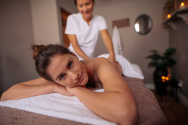 Attraktive Frau, die eine Rückenmassage in einem Spa-Center erhält. Frau, die eine Rückenmassage erhält und in die Kamera schaut, in einem Luxus-Spa. - JLPSF27595