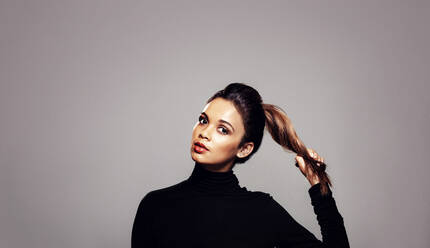 Strong healthy hair. Beautiful young woman holding her ponytail over grey background. - JLPSF27625