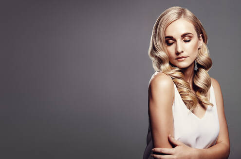 Schöne Frau mit langen blonden Haaren. Blondes Modell mit gewellter Frisur vor grauem Hintergrund mit Kopierraum. - JLPSF27628