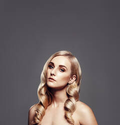 Quadratisches Porträt einer eleganten jungen Frau mit gewellter Frisur. Glamouröses weibliches Modell im Studio stehend vor grauem Hintergrund. - JLPSF27631