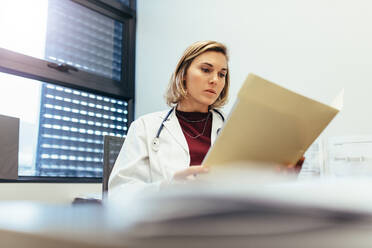 Eine Ärztin sitzt in ihrem Büro und studiert ihre Krankenakten. Ein Mediziner liest Berichte in einer Klinik. - JLPSF27649