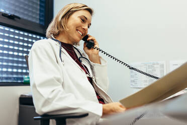 Eine Ärztin liest medizinische Berichte und telefoniert in einer Klinik. Ein Arzt arbeitet an seinem Schreibtisch. - JLPSF27650