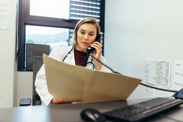 Ärztin, die Krankenakten liest und telefoniert. Medizinerin, die in ihrer Klinik Krankenberichte studiert und telefoniert. - JLPSF27651