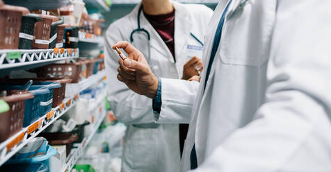 Two pharmacist looking for critical medicinal drug. Male doctor holding a medicine with female standing by in pharmacy. - JLPSF27679