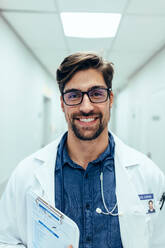 Portrait of happy doctor standing in hospital corridor. Caucasian man working in healthcare center. - JLPSF27683