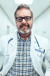 Porträt eines glücklichen und entspannten Arztes, der in einem Krankenhaus steht. Ein Mann im Laborkittel in einer Klinik schaut in die Kamera. - JLPSF27690