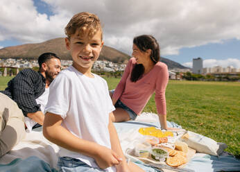 Cheerful couple with their child having a day out. Family sitting in a park with snacks for picnic. - JLPSF27694