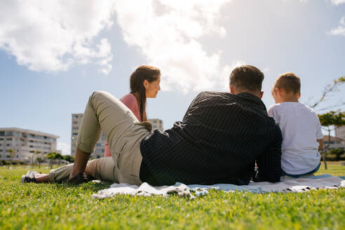 Rückansicht einer Familie, die in einem Park picknickt. Ein Paar mit seinem Kind, das einen Ausflug macht. - JLPSF27695