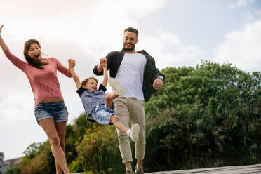 Glückliches Paar in spielerischer Stimmung im Freien mit ihrem Kind. Fröhliche Familie im Urlaub genießen im Freien. - JLPSF27698