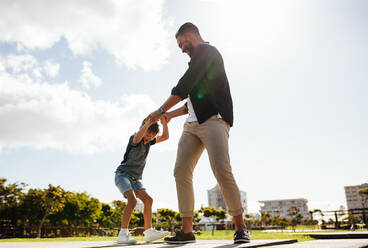 Fröhlicher Mann, der mit seinem Sohn im Park spielt. Vater hält die Hände seines Kindes in spielerischer Stimmung im Freien. - JLPSF27699