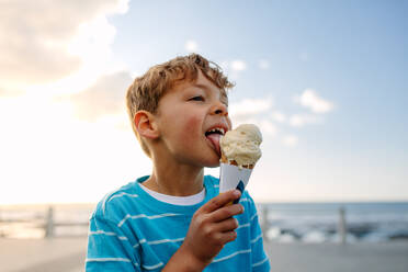 Junge isst ein Eis in der Nähe der Strandpromenade. Kleiner Junge im Urlaub, der sich ein Eis gönnt. - JLPSF27703