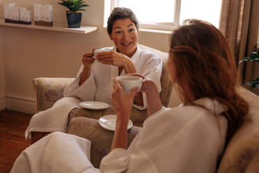 Two female friends drinking herbal tea and chatting in spa salon. Women relaxing at spa reception area. - JLPSF27716