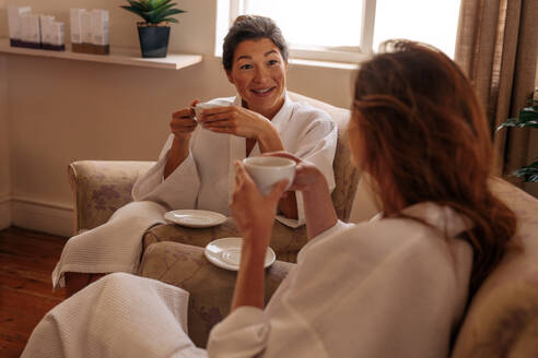 Zwei Freundinnen trinken Kräutertee und unterhalten sich im Spa-Salon. Frauen entspannen sich im Spa-Empfangsbereich. - JLPSF27716