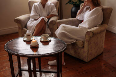 Spa reception area with women sitting in background waiting. Focus on table with candle and coffee cups. - JLPSF27720