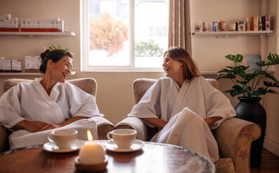 Female friends sitting in reception area and talking before spa treatment. Two young women relaxing in beauty spa waiting room and smiling. - JLPSF27722