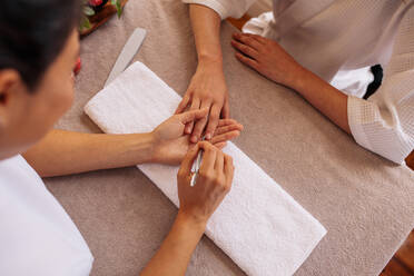 Draufsicht auf weibliche Hände in einem Salon, die von einer Kosmetikerin eine Maniküre und Nagelpflege erhalten. Maniküre mit einem Nagelhautschieber für eine Nagelmaniküre. - JLPSF27731