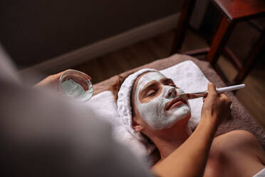 Beautiful woman receiving a face mask treatment at spa by therapist. Cosmetician applying facial mask on female face. - JLPSF27769