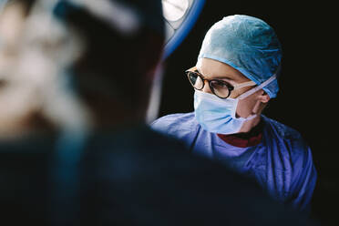 Chirurg mit medizinischer Maske und medizinischem Team, das eine Operation im Operationssaal eines Krankenhauses durchführt. - JLPSF27791