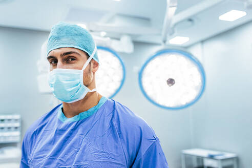 Porträt einer medizinischen Fachkraft mit chirurgischer Maske und Kittel im Operationssaal. Chirurg bereit für die Operation im Krankenhaus. - JLPSF27794
