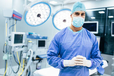 Portrait of male surgeon in operation theater looking at camera. Doctor in scrubs and medical mask in modern hospital operating theater. - JLPSF27795