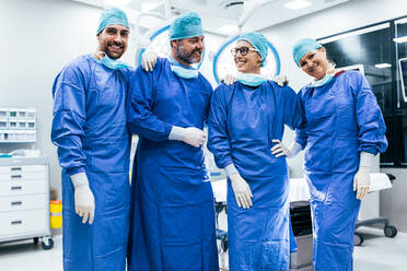 Porträt eines erfolgreichen Chirurgen-Teams, das im Operationssaal steht. Glückliche medizinische Mitarbeiter in chirurgischen Uniformen im Operationssaal. - JLPSF27799