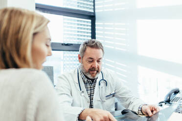 Mature doctor talking with female patient in clinic. Medical professional discussing diagnosis with patient in his office. - JLPSF27802