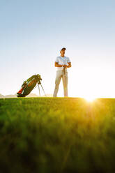 Niedrige Einstellung eines professionellen Golfspielers, der bei Sonnenuntergang auf einem Feld steht. Junger Mann spielt Golf auf einem Golfplatz. - JLPSF27821