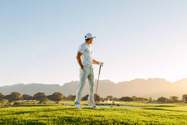 Voller Länge des jungen kaukasischen Mannes, der an einem Sommertag auf dem Golfplatz steht. Männlicher Golfer hält Golfschläger auf dem Feld. - JLPSF27825