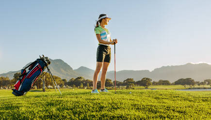 Totale Aufnahme einer Golferin auf dem Golfplatz, die auf den Abschlag wartet. Junge Frau hält einen Golfschläger und schaut an einem sonnigen Tag in die Ferne. - JLPSF27827