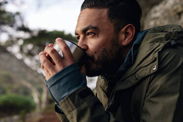 Close up shot of young man drinking hot coffee, taking break during hiking. Male hiker taking rest outdoors. - JLPSF27833