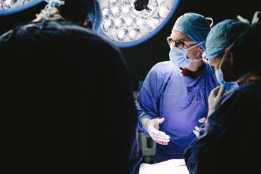 Surgeons team discussing during surgery. Group of doctors in hospital operation theater. - JLPSF27839