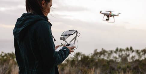 Junge Frau, die eine fliegende Drohne mit Fernbedienung steuert. Frau auf dem Lande, die Drohne fliegt und Fotos macht. - JLPSF27843