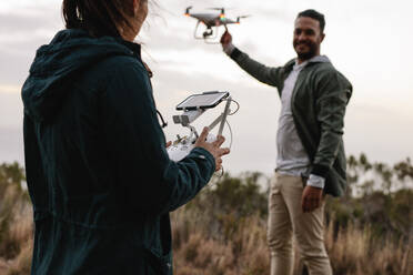 Frau mit Fernbedienung und Mann, der eine fliegende Drohne in der Landschaft hält. Junges Paar fliegt Drohne in der Landschaft. - JLPSF27844