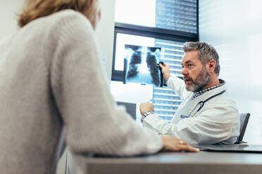 Ein Arzt zeigt seinem Patienten in einer Arztpraxis ein Röntgenbild. Ein Arzt sitzt mit seinem Patienten im Untersuchungsraum und bespricht die Diagnose des Röntgenbildes. - JLPSF27848